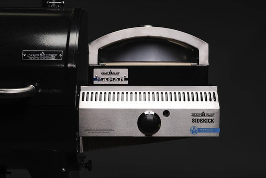 Close-up of a Camp Chef Sidekicks stainless steel grill accessory featuring a black lid, control knob, and grill vent set against a dark background.