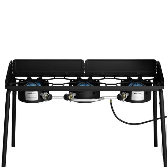 The Camp Chef Explorer is a double-burner outdoor gas stove with a sturdy metal frame, gas hose, side wind guards, and four legs—ideal for outdoor cooking adventures.