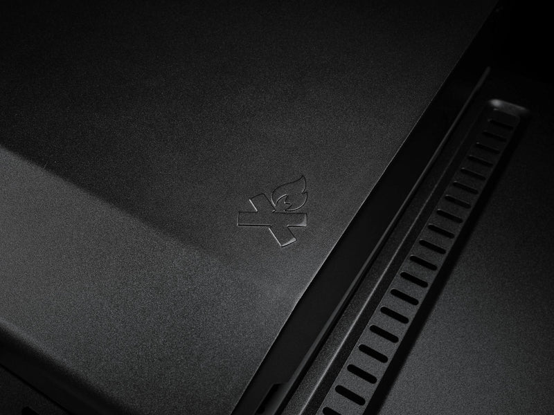 Load image into Gallery viewer, A close-up of the Camp Chef Gridiron 36’s matte black surface features an embossed campfire icon with a line through it, indicating no open flames. Vents on the right side provide even heating and simplify cleaning.
