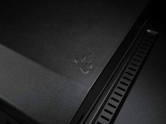 A close-up of the Camp Chef Gridiron 36’s matte black surface features an embossed campfire icon with a line through it, indicating no open flames. Vents on the right side provide even heating and simplify cleaning.