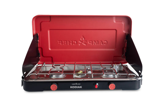 The Kodiak by Camp Chef is a compact camp stove featuring two burners, a red lid with the Camp Chef flame logo, a black base with red control knobs, and side wind guards—ideal for portable outdoor cooking.
