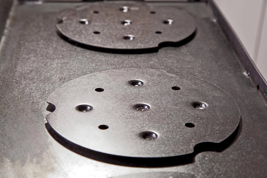 Close-up of a metal stovetop with two round, removable hot plates featuring holes and notches on a textured surface—ideal for use with the Camp Chef Griddles 16 or other professional griddle setups.
