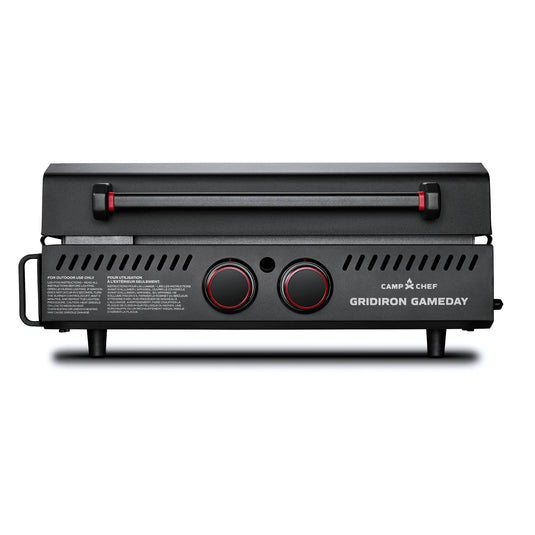 A black Camp Chef Gridiron Gameday portable grill with two red-accented knobs, a closed lid, side vents, and short legs is shown against a white background—perfect for outdoor cooking.