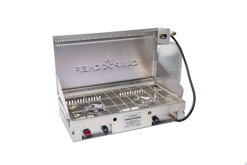 Load image into Gallery viewer, The Camp Chef Mountaineer outdoor cooking system, a stainless steel two-burner unit with an open lid and side-attached propane tank, is shown against a white background.
