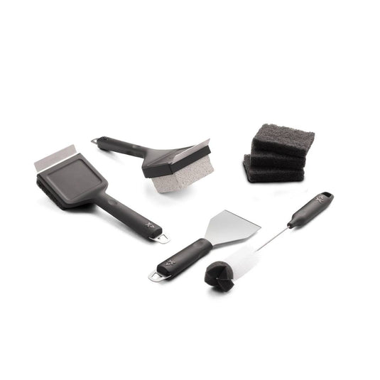 The Camp Chef Griddle Cleaning Kit includes five black-handled tools: two wire brushes, a griddle scraper, a stack of scouring pads, and a brush with a round scrubber, all shown on a white background.