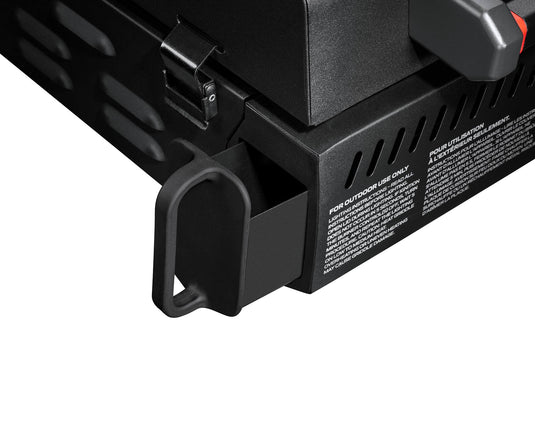 Close-up of the Camp Chef Gridiron Gameday portable tailgate grill, showcasing its rectangular pull-out tray and white-printed safety instructions on the side, highlighting key features of this outdoor cooking system.