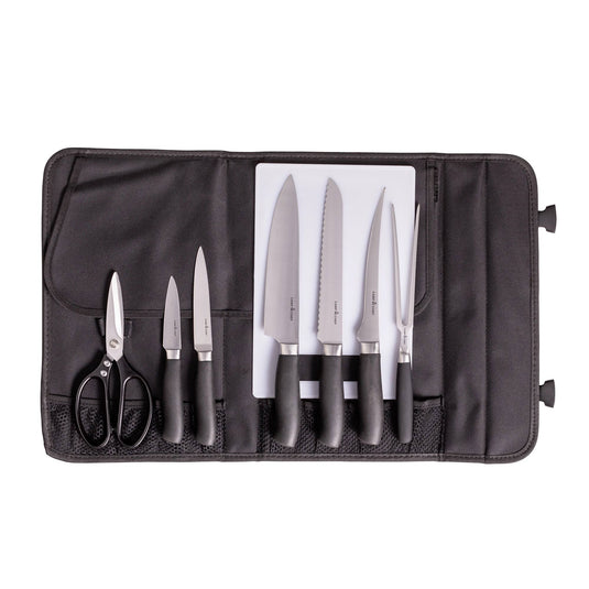 A black knife roll opens to display the Camp Chef 9 Piece Professional Knife Set, featuring six stainless steel kitchen knives, kitchen shears, and a white cutting board—all with black handles neatly organized in designated slots.