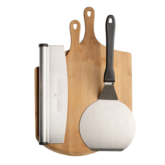 The Camp Chef Pizza Accessories Kit, featuring two wooden handled cutting boards, a metal dough scraper, and a metal pizza peel with black handle, is neatly displayed on a white background.