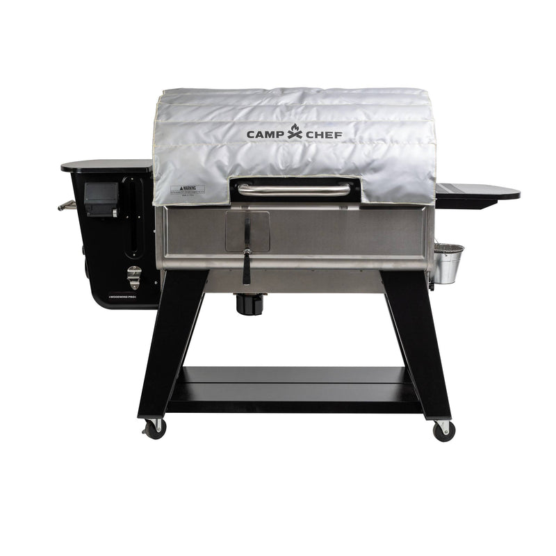 Load image into Gallery viewer, The Camp Chef Woodwind Pro with a silver, fire-resistant Woodwind Pro Blanket on the lid features a black frame, side shelves, and wheels for mobility.
