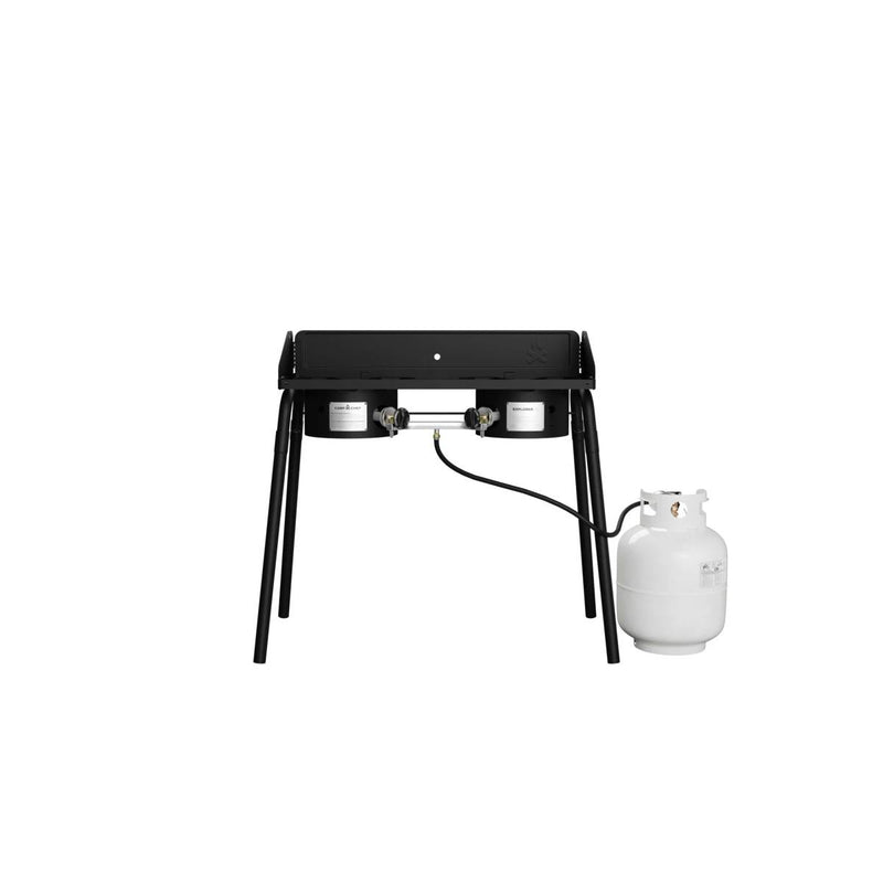 Load image into Gallery viewer, The Camp Chef Explorer, a black double-burner cooking system with four legs, is shown on a plain white background, connected to a white propane tank by hose—perfect for outdoor cooking.

