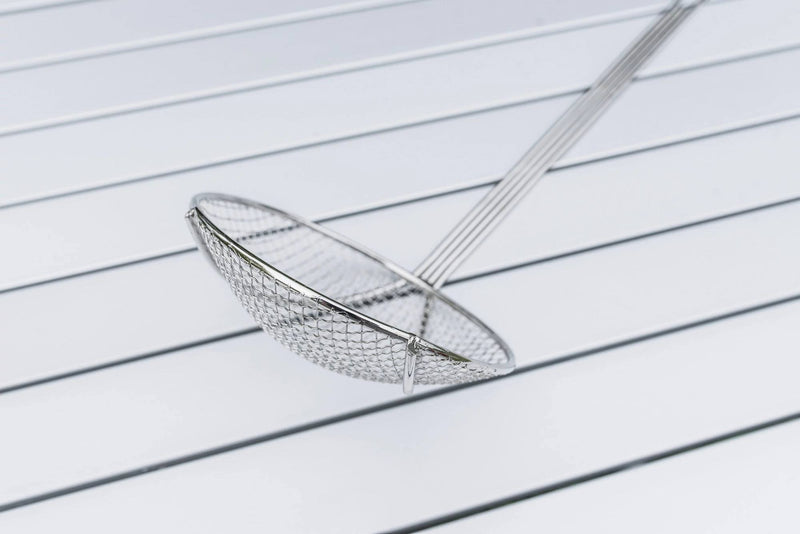 Load image into Gallery viewer, The Camp Chef Long Handled Skimmer, featuring a nickel-plated handle and round mesh basket, rests diagonally on a white slatted surface.
