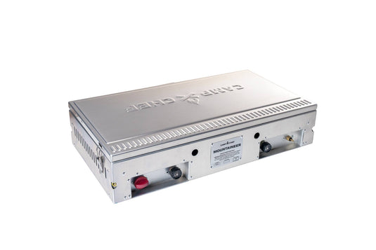 The Camp Chef Mountaineer is a durable rectangular metallic cooktop with two control knobs, side air vents, and the brand name engraved on the lid, shown resting on a white background.