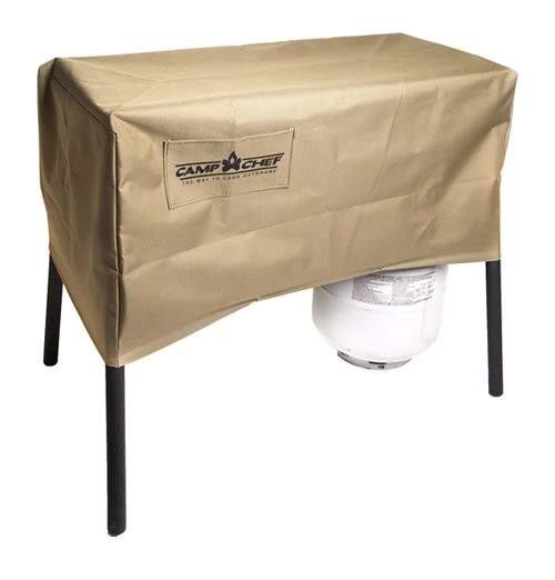 Load image into Gallery viewer, A tan, weather-resistant Camp Chef 14 IN Stove Cover protects an Explorer 3X grill or stove with black legs, partially hiding a white propane tank underneath.
