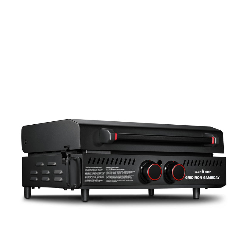 Load image into Gallery viewer, The Camp Chef Gridiron Gameday is a black rectangular portable tailgate grill with two red-accented front control knobs, a large cooking surface under the closed lid, short legs, and side vents for enhanced outdoor grilling.
