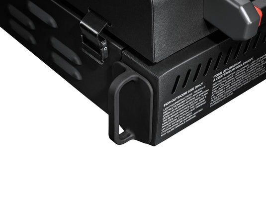 Close-up of the Camp Chef Gridiron Gameday, a black metal portable tailgate grill with vent holes, latch, handle, and safety instructions in white—ideal for any outdoor cooking setup.