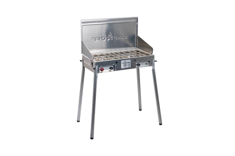Load image into Gallery viewer, The Camp Chef Mountaineer is a silver, freestanding outdoor cooking system with four legs, wire cooking grate, side and back panels, control knobs, and a front label.
