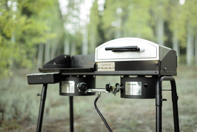 Portable grill with pizza oven attachment in a forest setting