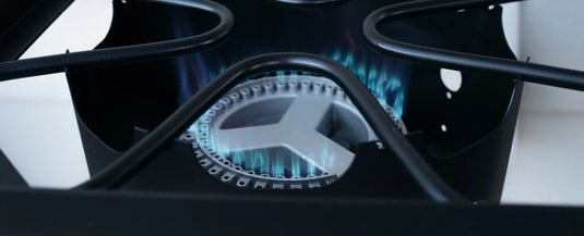 A close-up view of a lit gas stove burner with blue flames evenly circulating around the metal burner beneath a black stove grate.