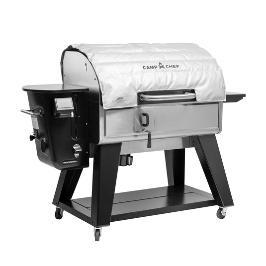 The Camp Chef Woodwind Pro Blanket is a fire-resistant white fiberglass cover for the stainless steel Woodwind grill, featuring a black frame, left-side control panel, and four wheels for easy mobility.