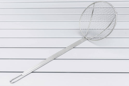 The Camp Chef Long Handled Skimmer, featuring a round fine wire mesh basket and nickel plated handle, rests on a white slatted surface.