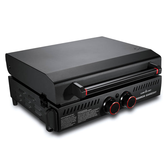 The Camp Chef Gridiron Gameday is a compact black tabletop gas grill with a closed lid and two front control knobs, making it the perfect portable tailgate grill for outdoor cooking anywhere.