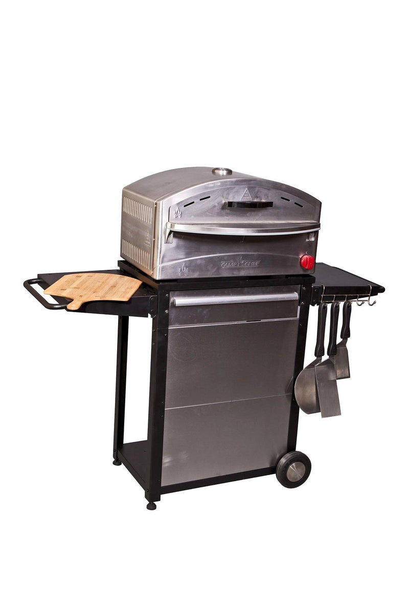 Load image into Gallery viewer, The Camp Chef Patio Cart is a stainless steel kitchen cart pizza oven with wheels, side shelves, a wooden cutting board, and hanging utensils—ideal for any outdoor kitchen or patio setup. Isolated on a white background.
