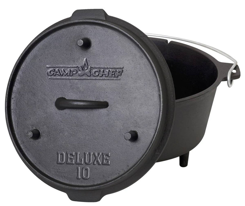Load image into Gallery viewer, The Camp Chef Deluxe Dutch Oven is a black cast iron pot featuring a lid with embossed text, short legs, and a metal carrying handle. The lid is shown tilted against the pot.
