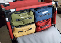 A fabric organizer with four colorful storage bins—green, blue, yellow, and red—sits on carpet. The bins have black handles and clear label slots, and the frame is black with red accents.